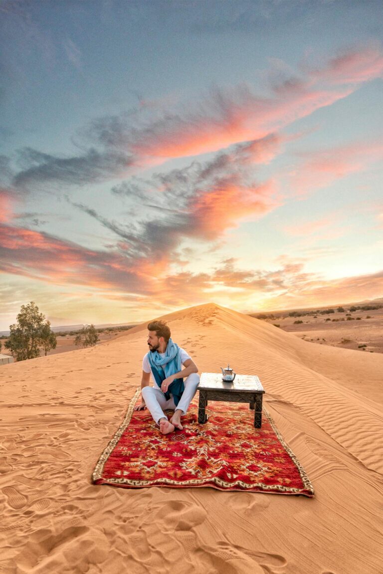 Serene image of a person relaxing on a carpet in the Moroccan desert at sunrise.