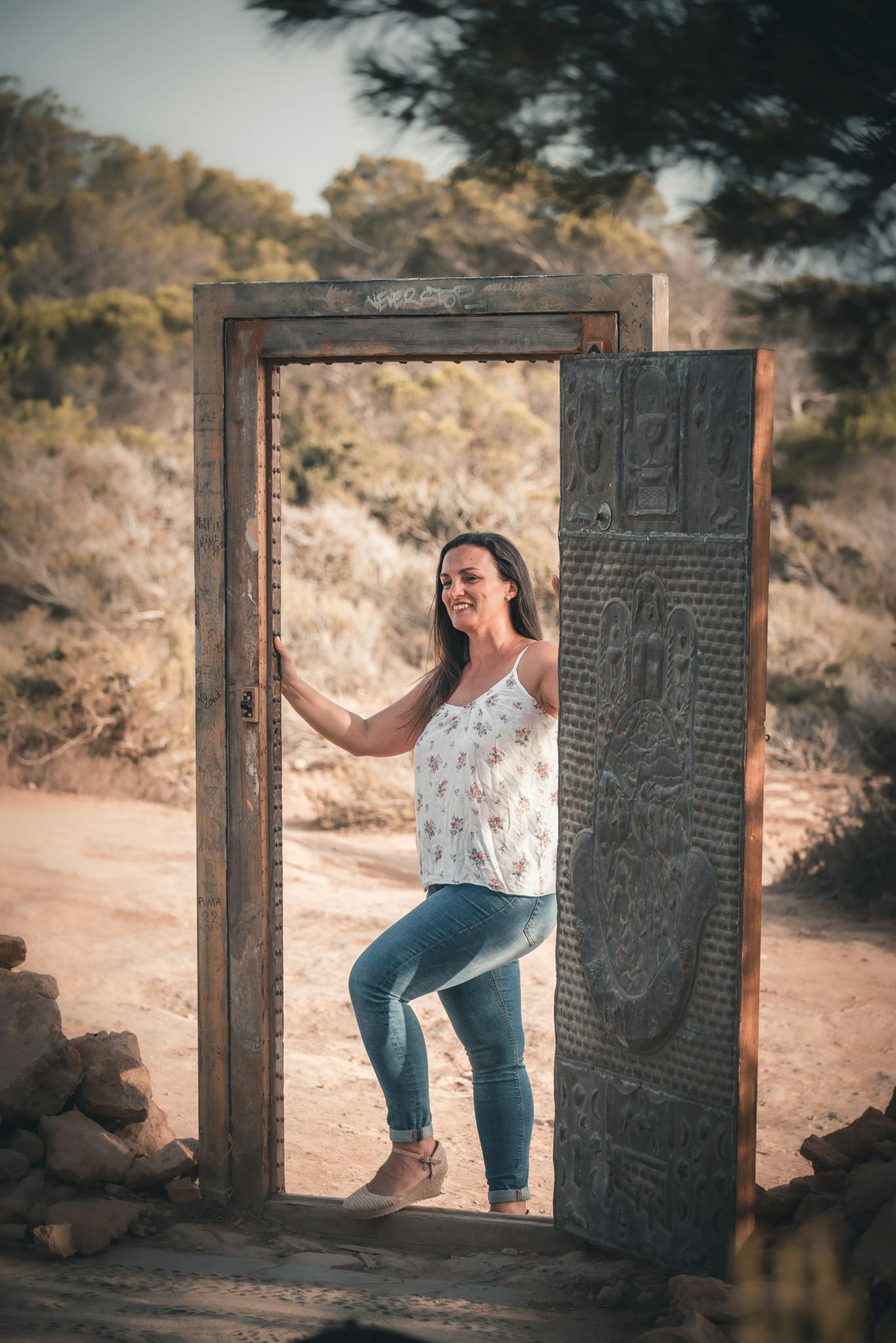 Smiling woman posing in an antique door frame surrounded by nature.